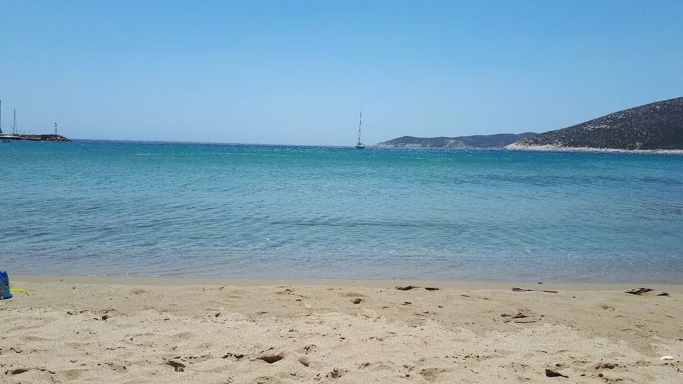Platis Gialos beach, Sifnos, on a clear summer day: calm turquoise water and a sailboat anchored off the sand