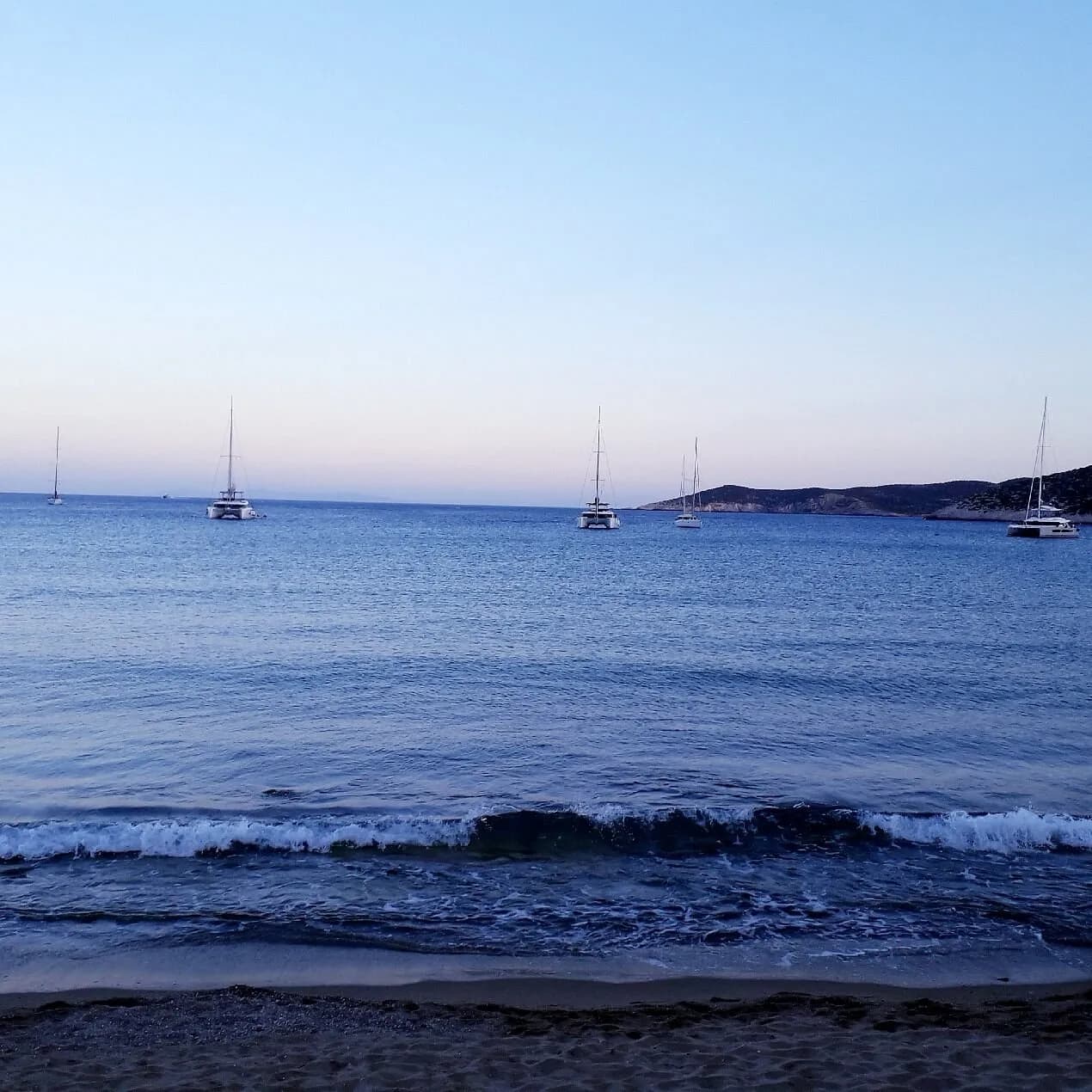 Yachts at anchor off an empty Platis Gialos beach at dusk, Sifnos